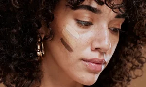Woman applying liquid foundation with a makeup sponge, demonstrating a flawless, natural finish.